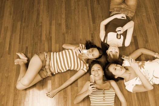 High angle view of four young women lying on a hardwood floor and holding their mobile phones