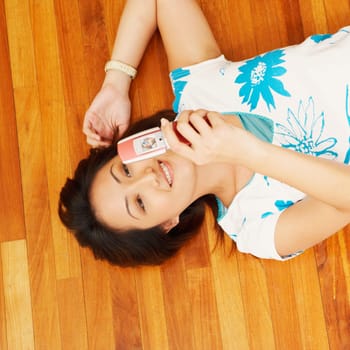 High angle view of a young woman lying on a hardwood floor and holding a mobile phone