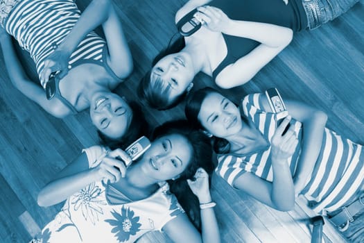 High angle view of four young women lying on a hardwood floor and holding their mobile phones