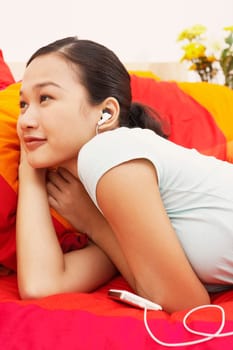 Young woman lying on the bed and listening to music on headphones