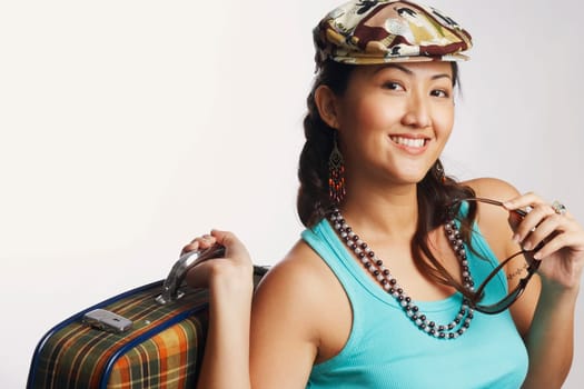 Portrait of a young woman holding sunglasses and a suitcase