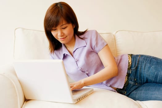 Young woman lying on a couch and working on a laptop