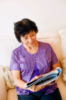 Mature woman sitting on a couch and reading a magazine