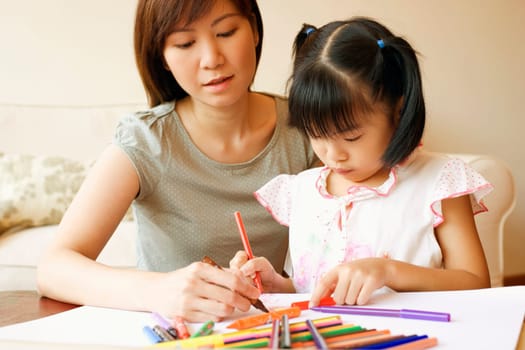 Close-up of a young woman teaching her daughter to color