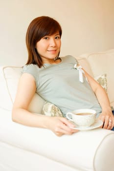 Portrait of a young woman sitting on a couch and holding a cup of tea