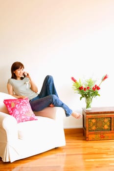 Young woman sitting in an armchair and talking on a mobile phone
