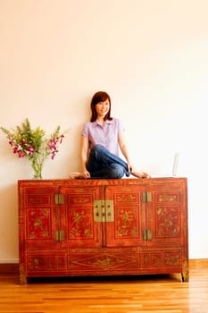 Portrait of a young woman sitting on a cabinet with a laptop beside her