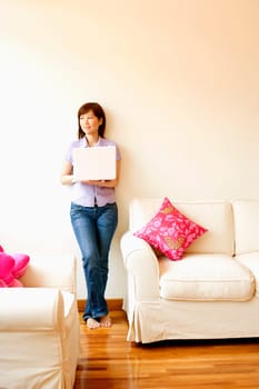 Young woman leaning against a wall and holding a laptop