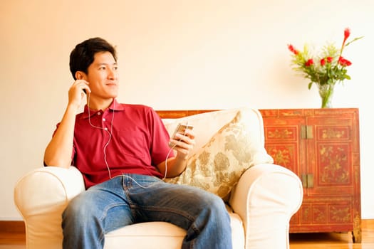 Young man sitting on an armchair and listening to an MP3 player