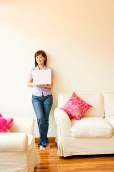 Young woman leaning against a wall and holding a laptop