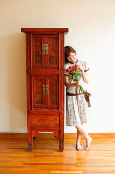 Close-up of a young woman standing near a cabinet and holding a bouquet of red roses