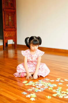 Close-up of a girl sitting on the floor and playing with a jigsaw puzzle
