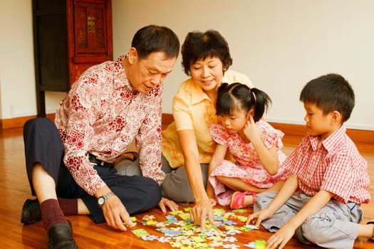 Boy with a girl and their grandparents playing with a jigsaw puzzle