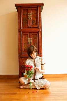 Close-up of a young woman sitting on the floor and plucking a rose