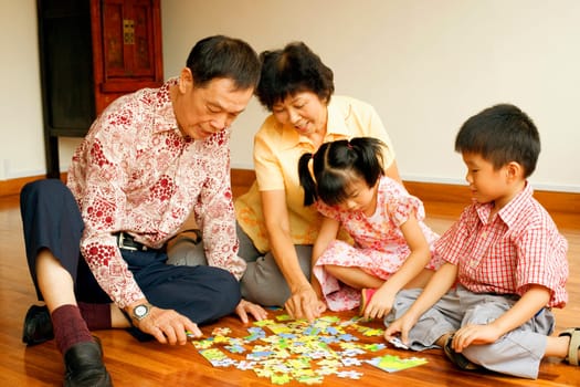 Girl and a boy playing jigsaw puzzle with their grandparents