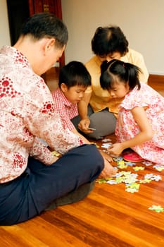 Boy with a girl and their grandparents playing with a jigsaw puzzle