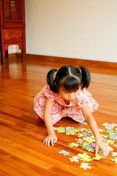 Close-up of a girl sitting on the floor and playing with a jigsaw puzzle