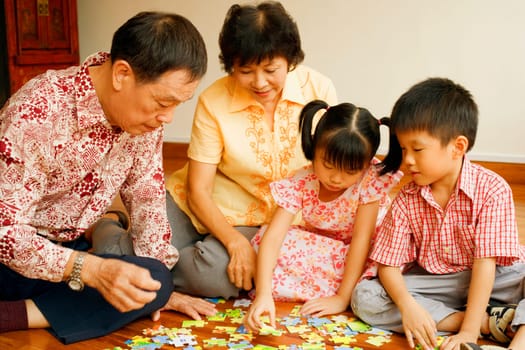 Boy with a girl and their grandparents playing with a jigsaw puzzle