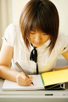 Close-up of a young woman writing on a notepad in a classroom