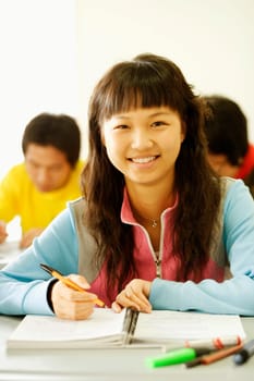 Portrait of a young woman sitting at a desk in the classroom and smiling