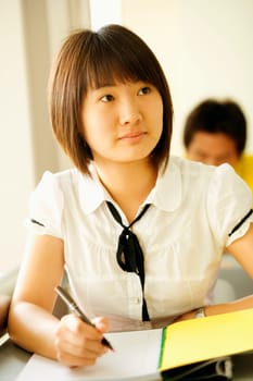 Close-up of a young woman writing on a notepad in a classroom