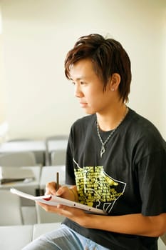 Close-up of a teenage boy writing on a notepad and sitting in the classroom