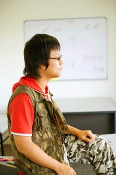 Side profile of a teenage boy sitting on a desk in a classroom