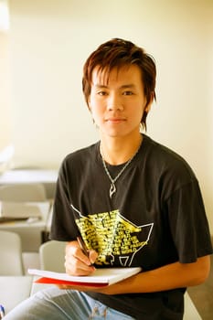 Portrait of a teenage boy holding a pen on a notepad in a classroom