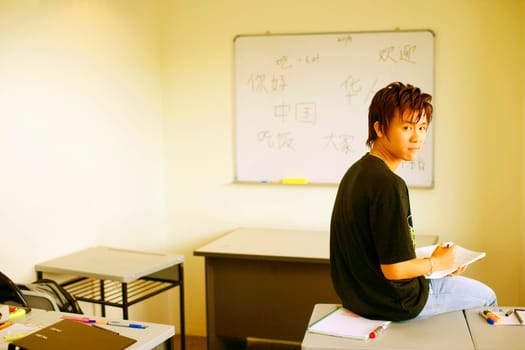 Side profile of a teenage boy sitting on a desk in a classroom