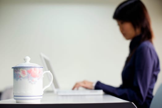 Close-up of a kettle and a young woman using a laptop