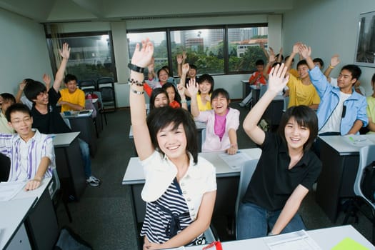 Close-up of students sitting in a classroom and raising their hands