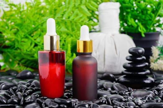 Thai Spa massage setting with red serum oil bottle dropper mock up or essential oil on black stone