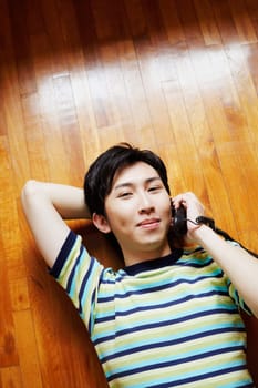 High angle view of a young man talking on the telephone and lying on a hardwood floor