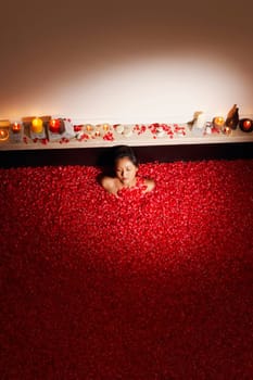 High angle view of a young woman in a bath tub full of rose petals with her eyes closed