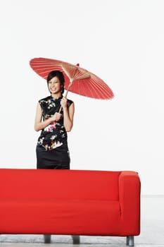 Portrait of a young woman standing behind a couch holding a parasol