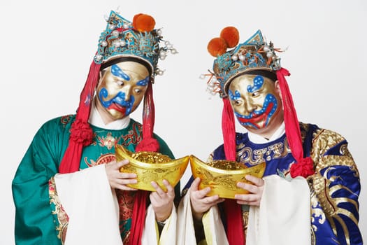 Close-up of two male Chinese opera performers looking at bowls full of gold coins