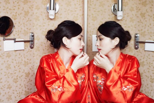 Young woman looking in the mirror applying lipstick