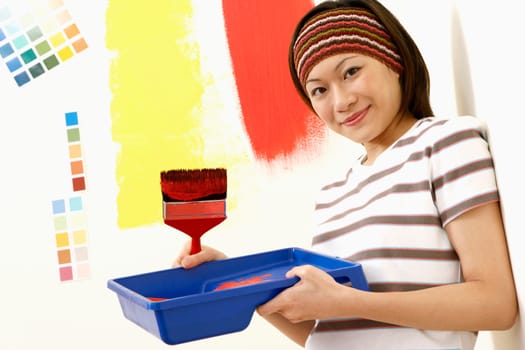 Portrait of a young woman holding a paint tray with a paintbrush and smiling