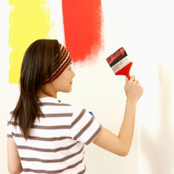 Rear view of a young woman painting the wall with a paintbrush