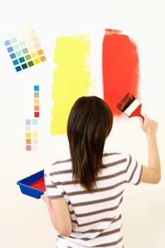 Rear view of a young woman painting the wall with a paintbrush