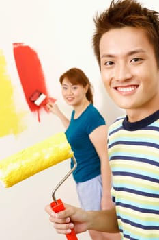 Portrait of a young man holding a paint roller with a young woman standing in the background
