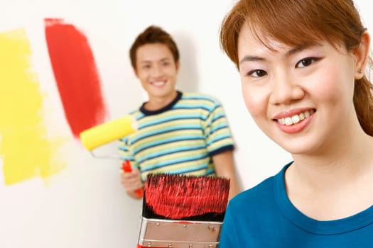 Portrait of a young woman holding a paintbrush with a young man standing in the background