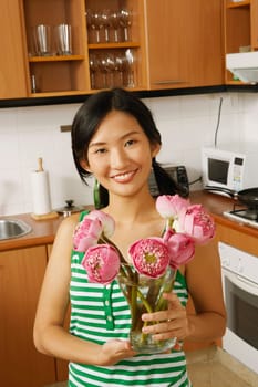 Portrait of a young woman holding a flower vase in the kitchen