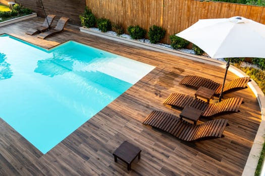 Elegant poolside wooden deck with lounge chairs, umbrella, and turquoise swimming pool in a serene backyard