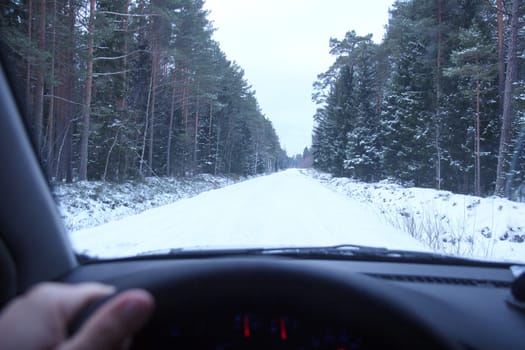 Winter Driving. Driving car through forest by small snowy road.
