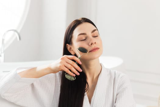 Beautiful european woman uses jade roller to massage her face. Spa self beauty procedure