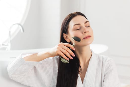 Beautiful european woman uses jade roller to massage her face. Spa self beauty procedure