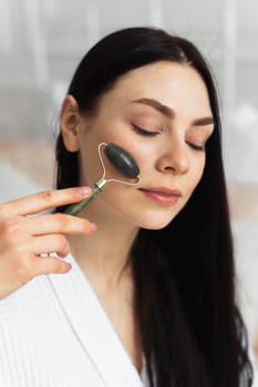 Beautiful european woman uses jade roller to massage her face. Spa self beauty procedure