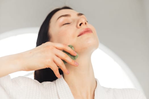 Young woman doing face Gua sha - chinese traditional massage
