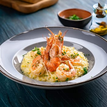 Risotto aux gambas features creamy Arborio rice topped with grilled prawns and garnished with colorful accents for an indulgent experience.